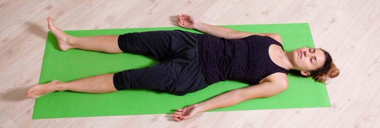 Woman lying on a green yoga mat in a relaxation pose