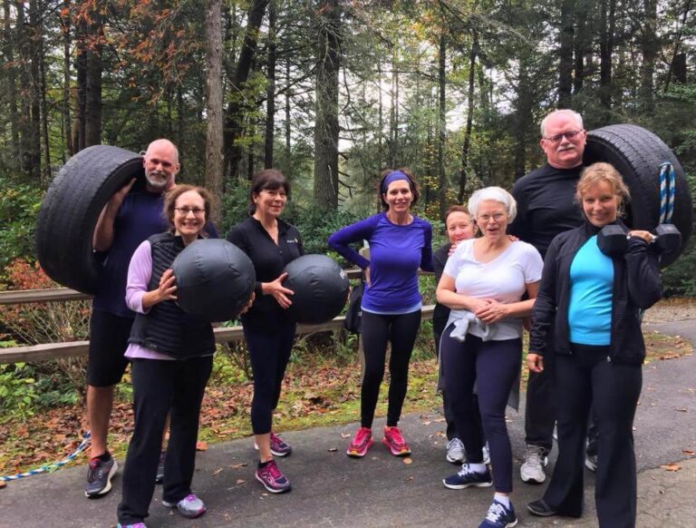 Smiling group of guests holding medicine balls on a wooded road