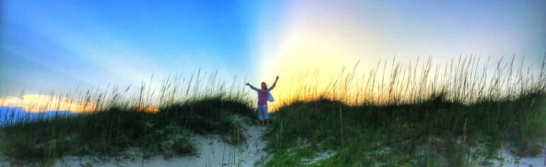 Person with raised arms on a beach dune at sunrise