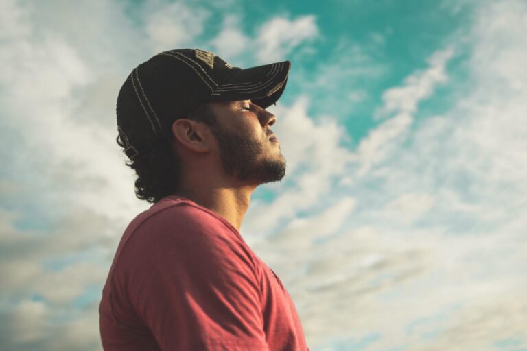 Man in a cap breathing deeply with eyes closed under a cloudy sky