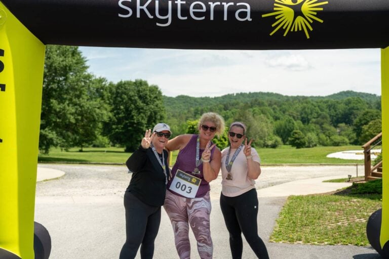 Three smiling runners under the Skyterra 5K finish arch