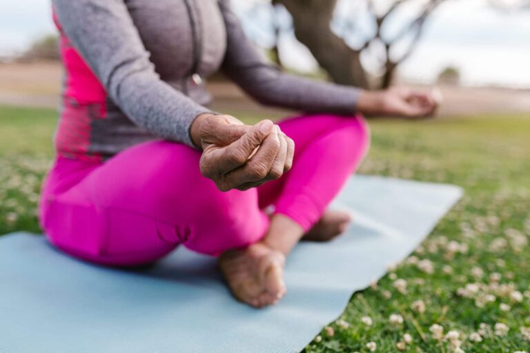 Woman in pink leggings meditating cross-legged on a mat outdoors