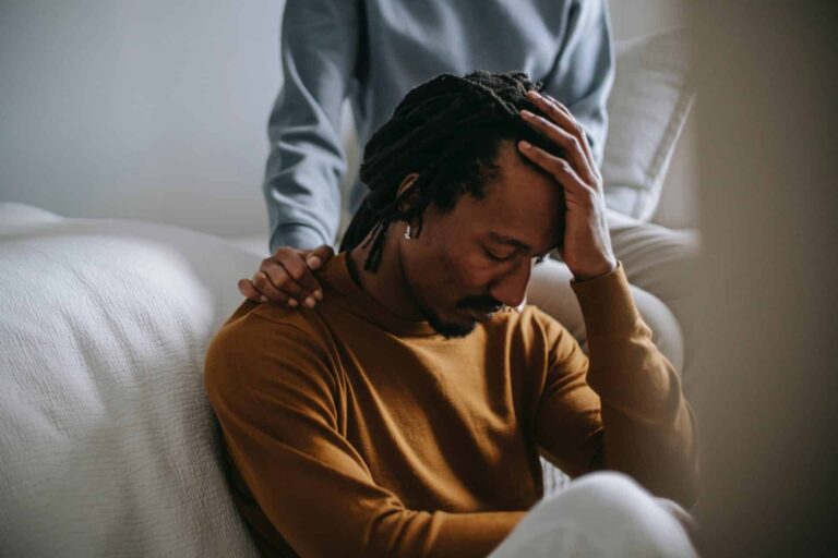 Man holding his head in grief as someone rests a hand on his shoulder