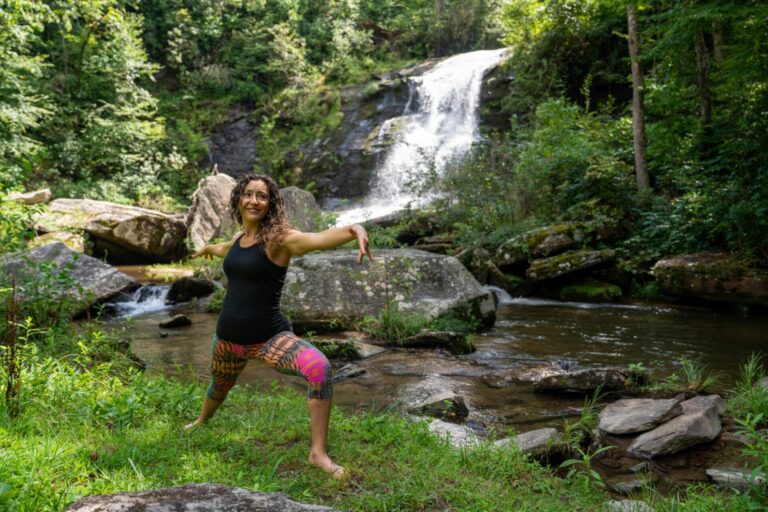 Guest holding a yoga pose on the grass beside a mountain waterfall