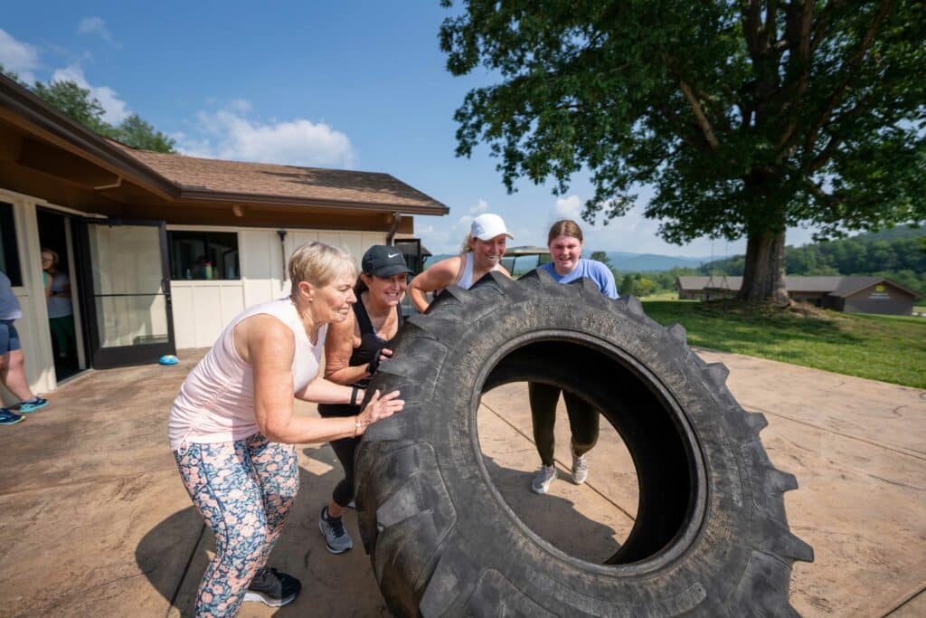 Guests working together to flip a large tractor tire during an outdoor fitness class