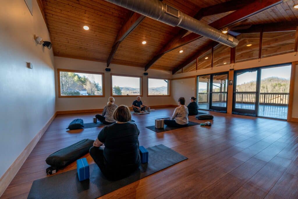 Guests meditating on cushions in a wood-beamed studio with mountain views