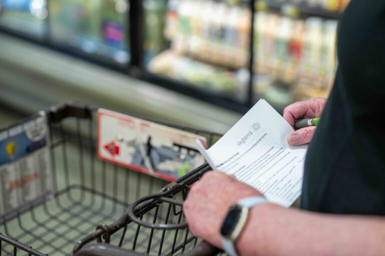 Shopper holding a grocery list beside a shopping cart