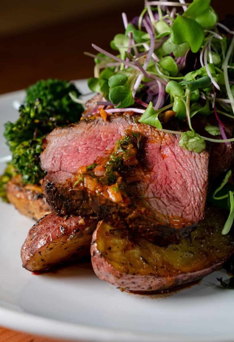 Chef-prepared plate of sliced steak, roasted potatoes, broccolini and microgreens