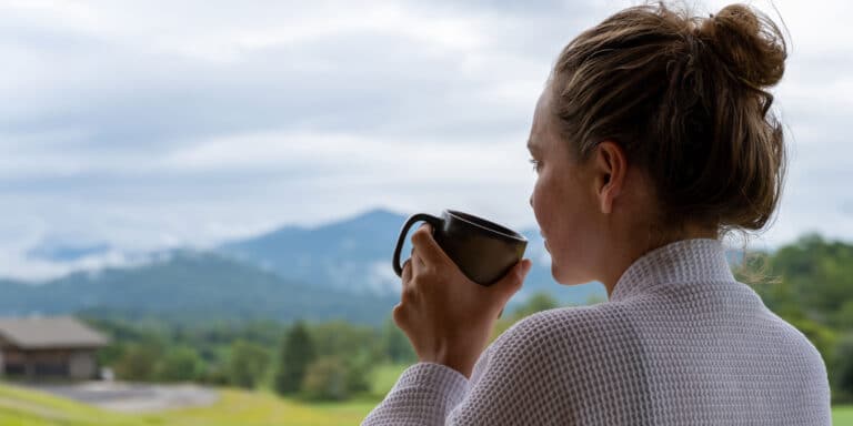 Guest relaxing with a warm drink and a misty mountain view
