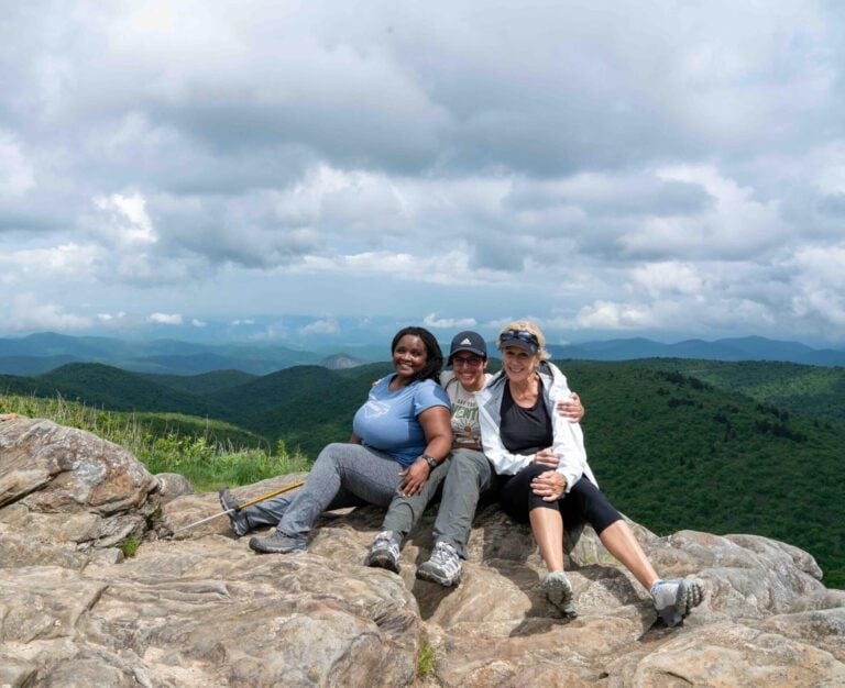 Three guests sitting on a rocky summit above Blue Ridge ridgelines