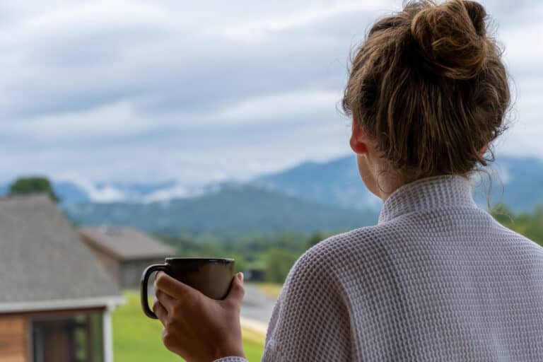 Guest holding a mug of coffee and looking out at the Blue Ridge Mountains